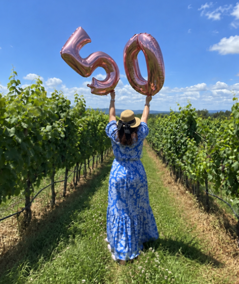 A woman in a vineyard holding fiftieth birthday balloons