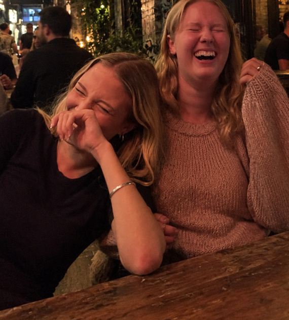 Two women cracking up laughing at a bar table