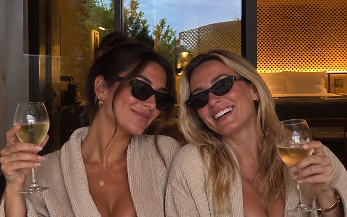Two friends in robes and sunglasses toasting with white wine on a girls sleepover weekend