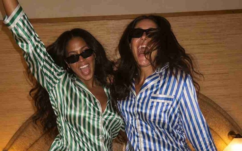 Two friends in silk pyjamas and sunglasses dancing on the bed