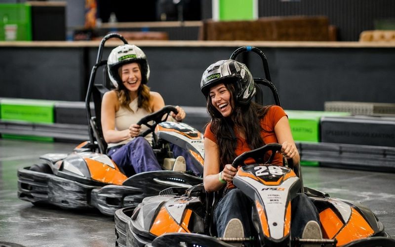 Two friends laughing in helmets in their e karts on an indoor track on a Sydney girls weekend