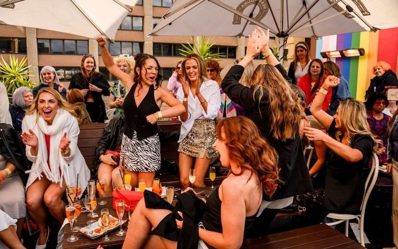 The girls up on their feet cheering and dancing at a rooftop drag brunch on a Sydney girls weekend