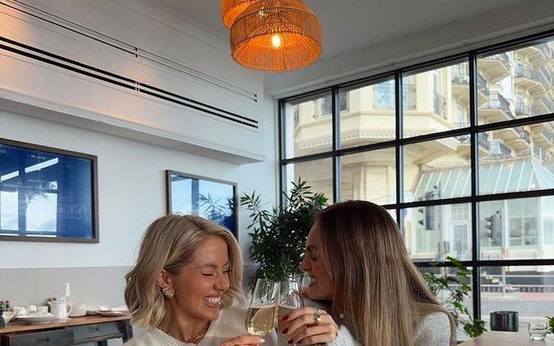 Two friends toasting and laughing over brunch drinks at a bright restaurant on a Sydney girls weekend