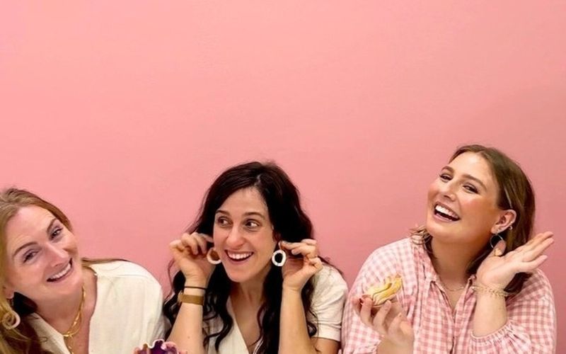 Three friends laughing and showing off their clay pieces against a pink wall on a Sydney girls weekend
