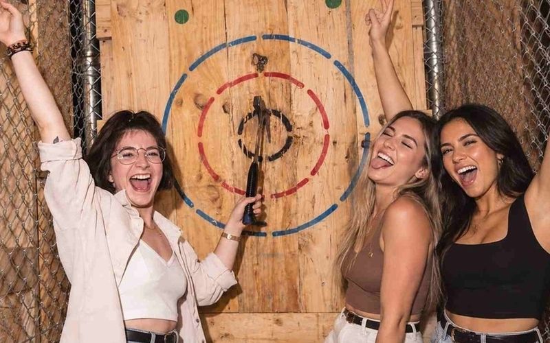 Three friends cheering beside a bullseye during an axe throwing tournament on a Sydney girls weekend