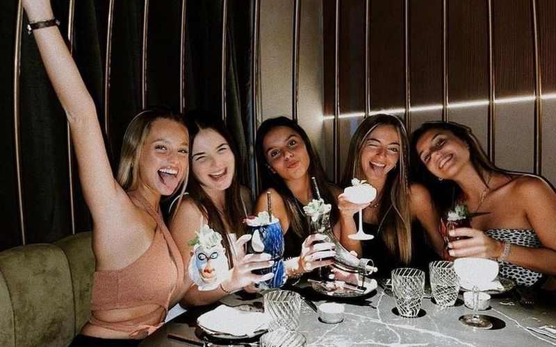 The girls raising their glasses in a moody booth at a wine tasting on a Sydney girls weekend