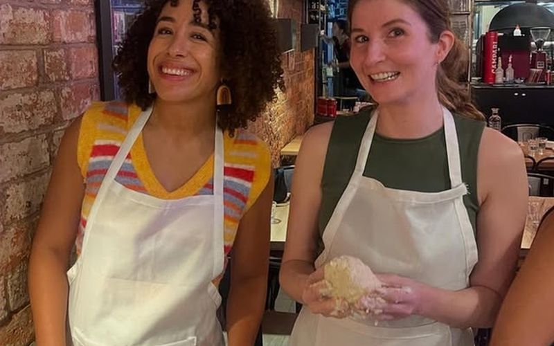 Two friends in aprons grinning with fresh gnocchi dough in their hands at a masterclass on a Melbourne girls trip