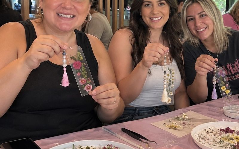 Three friends proudly holding up the bookmarks they made at a craft workshop on a Melbourne girls weekend