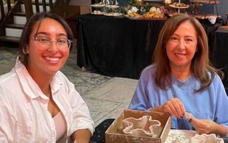 Two friends smiling over their clay pieces at a pottery workshop table on a Melbourne girls weekend