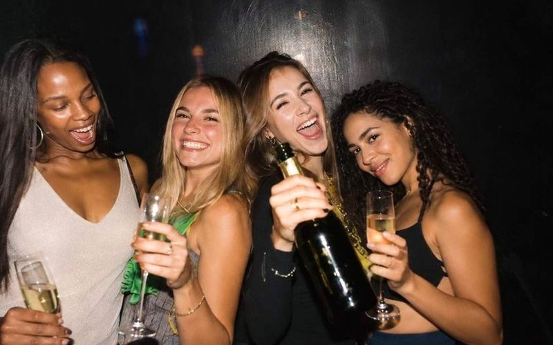 Four friends laughing with a bottle of bubbly and full glasses in their booth on a Melbourne girls trip