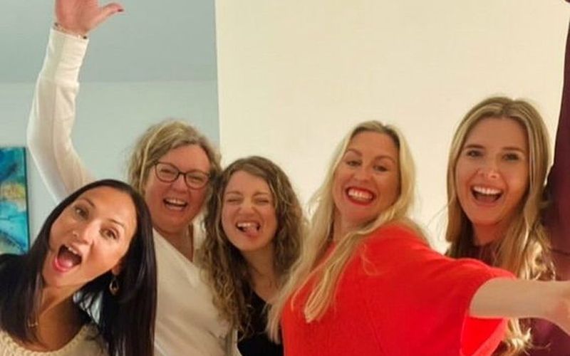 Five friends cheering and waving for a group selfie at the apartment on a Brisbane girls trip