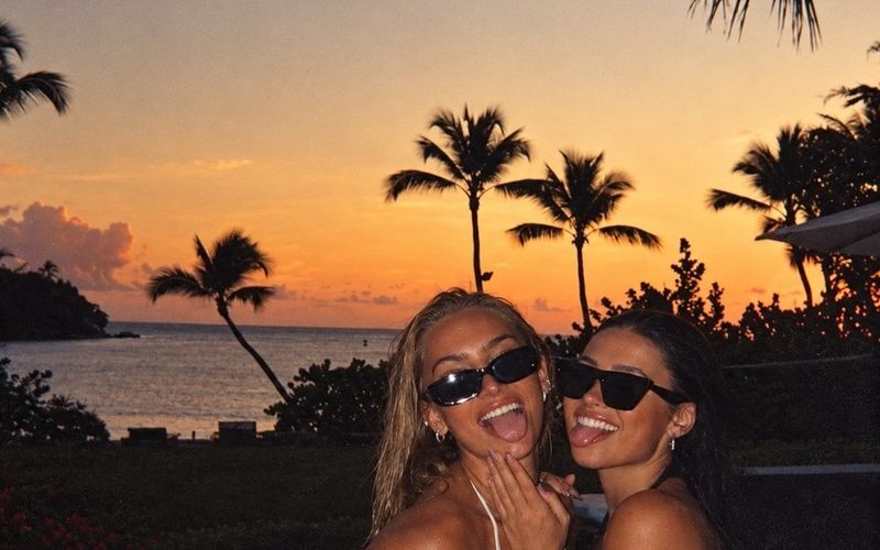 Two friends in sunglasses laughing together under palm trees at sunset on a Brisbane girls trip