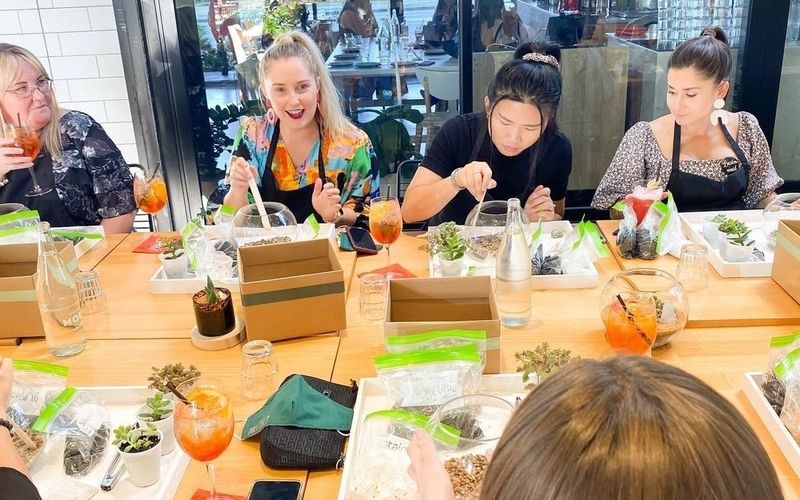 Friends potting tiny succulents into glass terrariums around the workshop table on a Brisbane girls trip