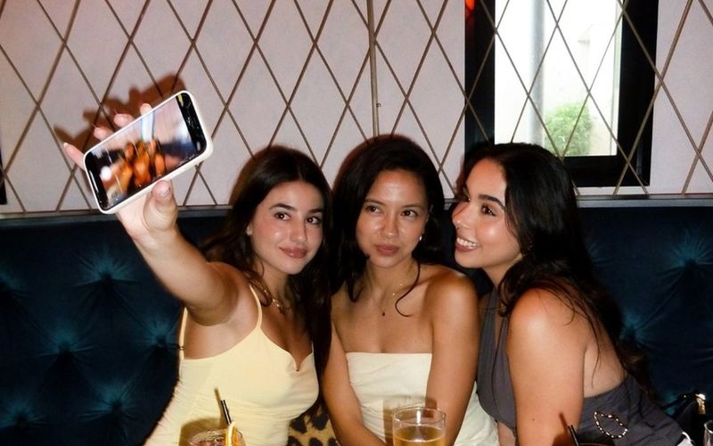 Four friends with colourful cocktails snapping a selfie in a velvet booth on a Brisbane girls weekend