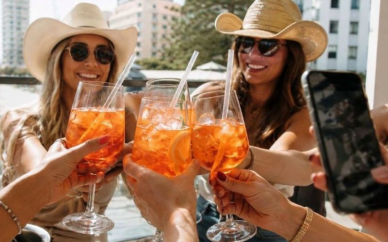 Friends in cowboy hats clinking drinks on a sunny terrace on a Brisbane girls trip