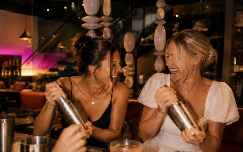 Two friends laughing as they shake cocktails at the bar during a private class on a Gold Coast girls weekend
