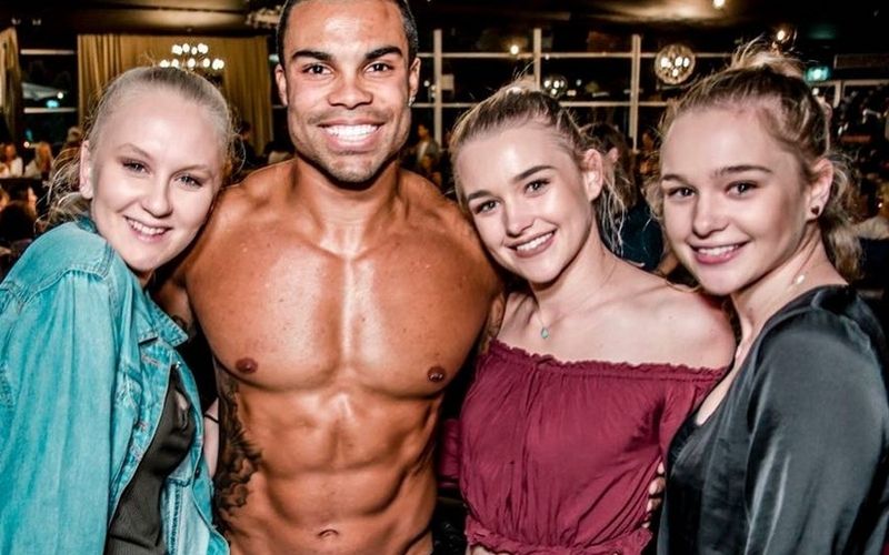 Three friends grinning with a smiling topless waiter on a Gold Coast girls weekend