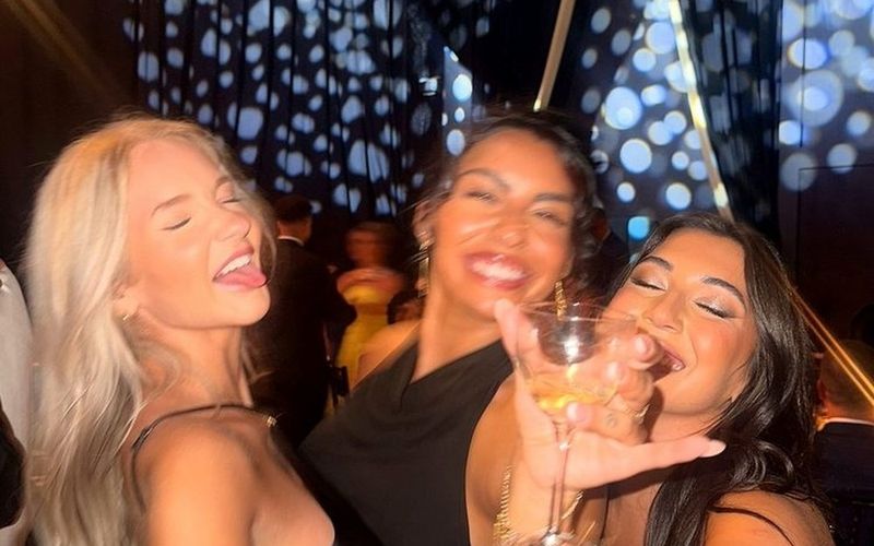 Three friends cheering with glasses raised toward the camera in a nightclub on a Gold Coast girls weekend