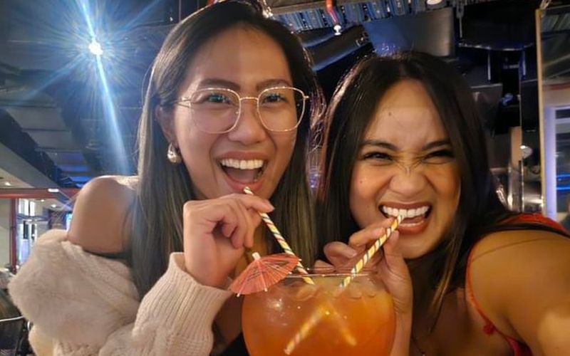 Two friends laughing as they share a big cocktail through two straws at a lively bar on a Gold Coast girls weekend