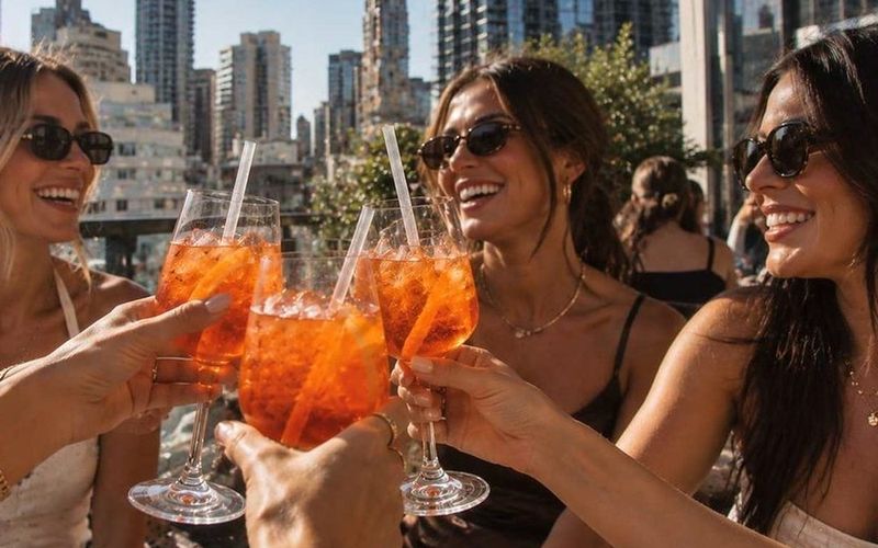 Friends in sunglasses clinking drinks against a city skyline on a Gold Coast girls weekend