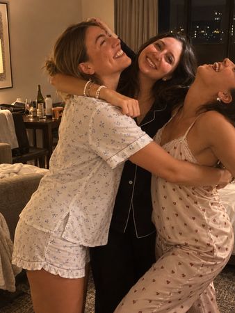 Three friends in pyjamas tangled in a laughing hug in a hotel room