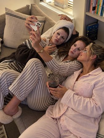 Three friends in pyjamas and sheet masks taking a selfie on the sofa