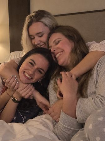 Three friends in pyjamas piled together on a hotel bed