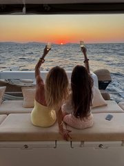 Two friends raising champagne to the sunset from the back of a yacht