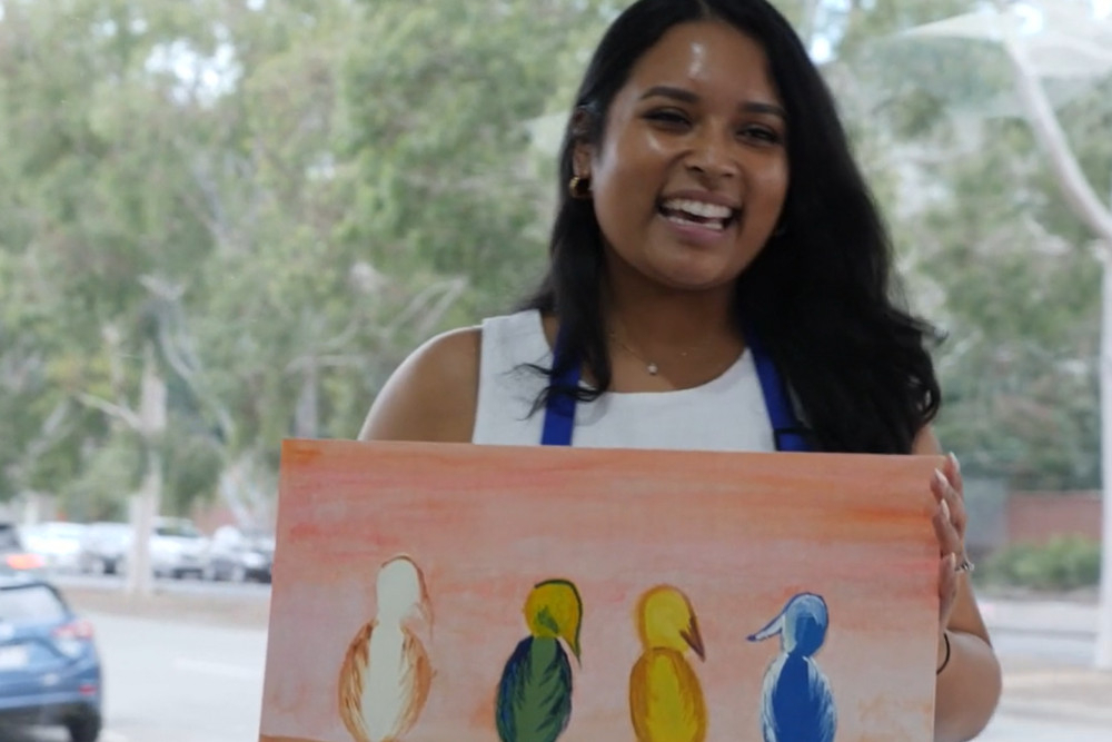 A laughing painter holding up her painting of four birds on a wire