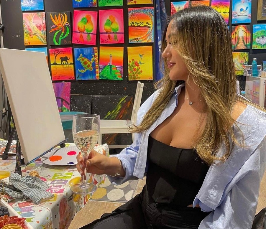 A friend with a glass of bubbles eyeing her blank canvas in a studio hung with bright paintings