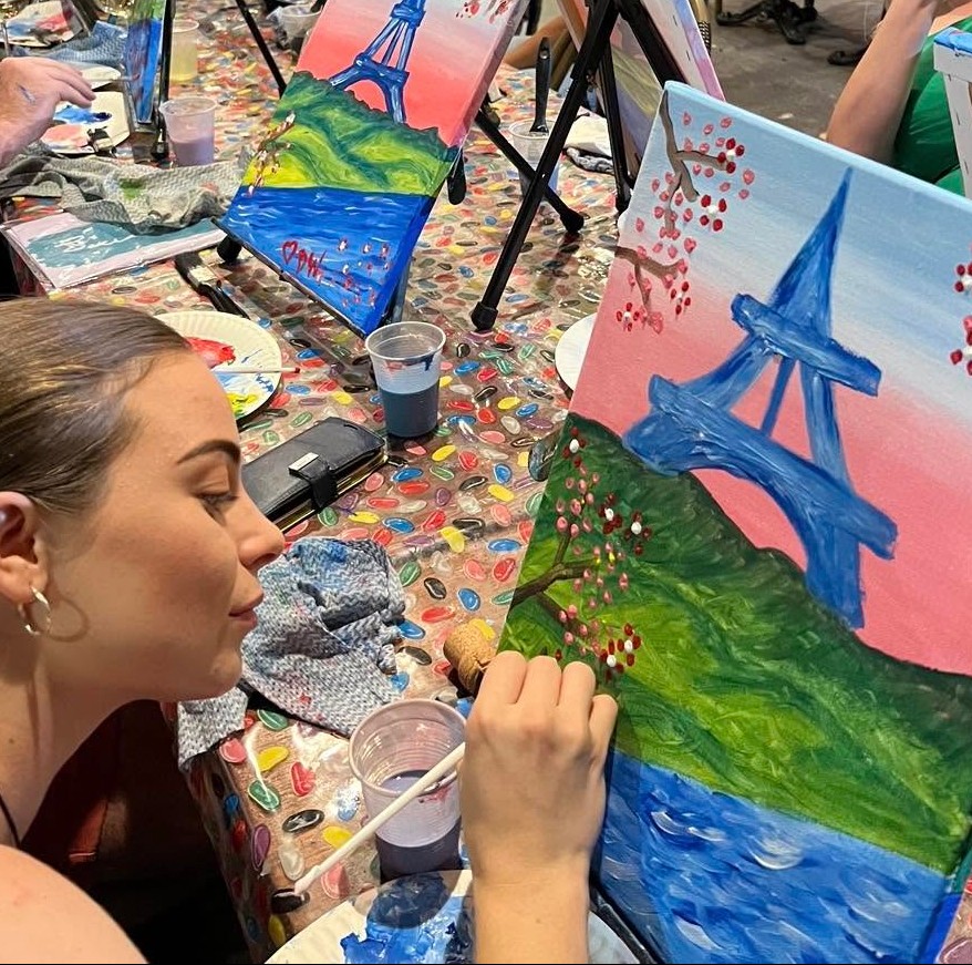 A painter leaning in to add cherry blossoms around a pink and blue Eiffel Tower