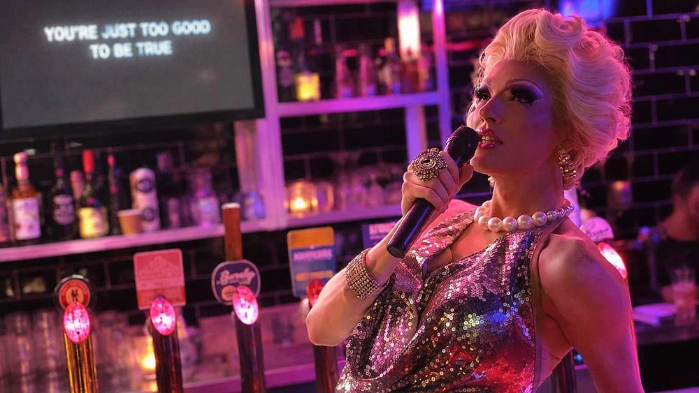 A drag performer in sequins and pearls singing at a bar