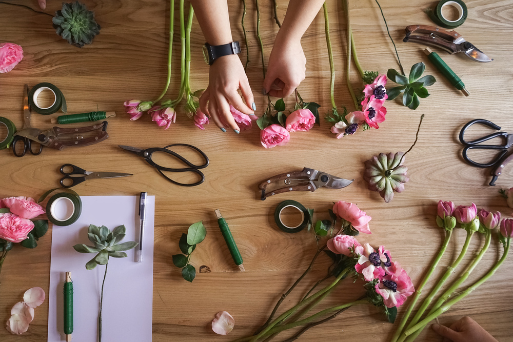 Hands arranging pink roses and anemones on a florist’s timber workbench