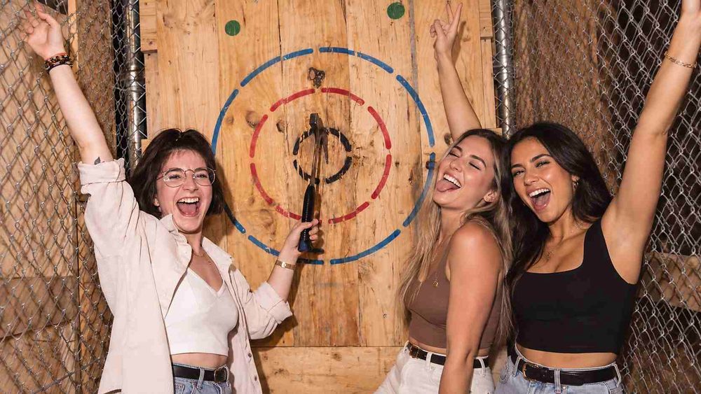 Three friends cheering in front of an axe throwing target