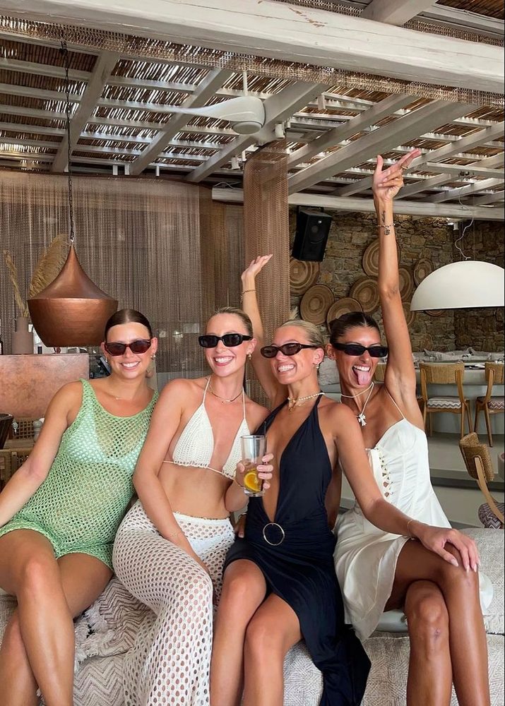 Four friends in sunglasses laughing on a daybed at a beach club
