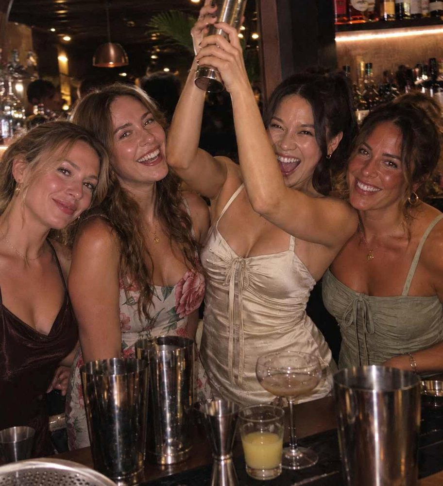 Five friends cheering behind a bar with a cocktail shaker held up