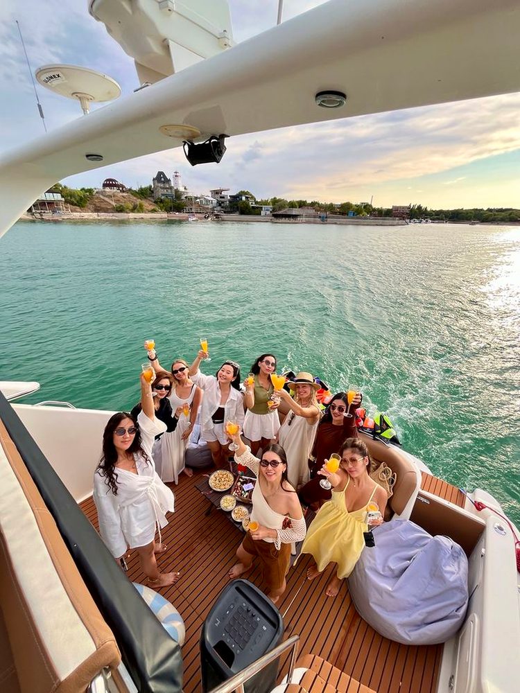 A big group of friends raising mimosas on the back deck of a boat over turquoise water