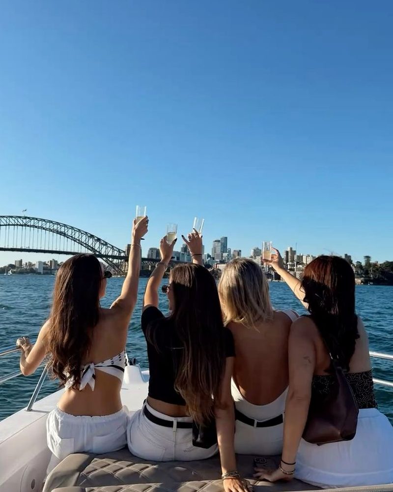 Four friends on the bow of a boat raising glasses towards the Sydney Harbour Bridge