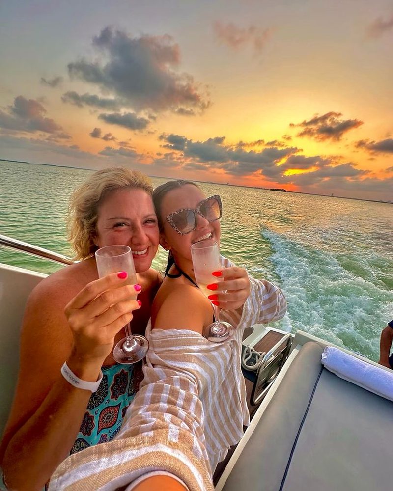 Two friends of different ages clinking champagne on a boat at sunset