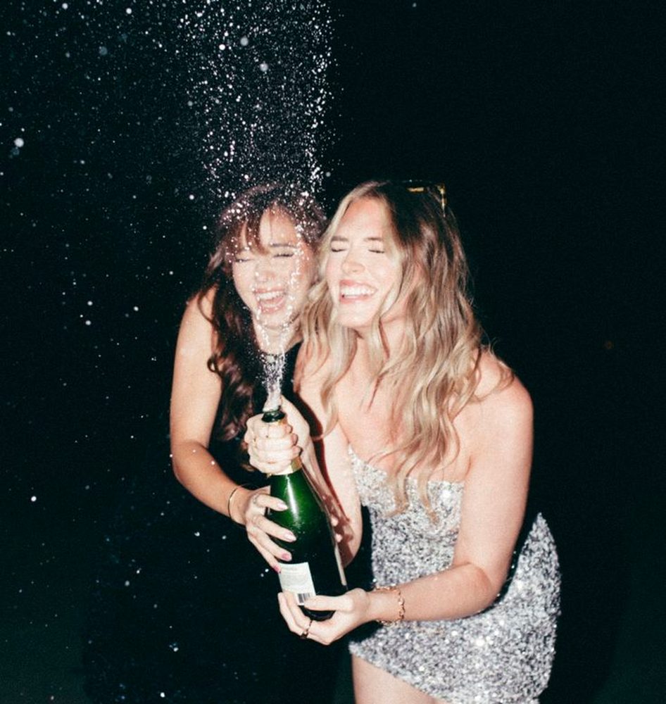 Two friends laughing as a bottle of bubbles sprays into the air on a night out