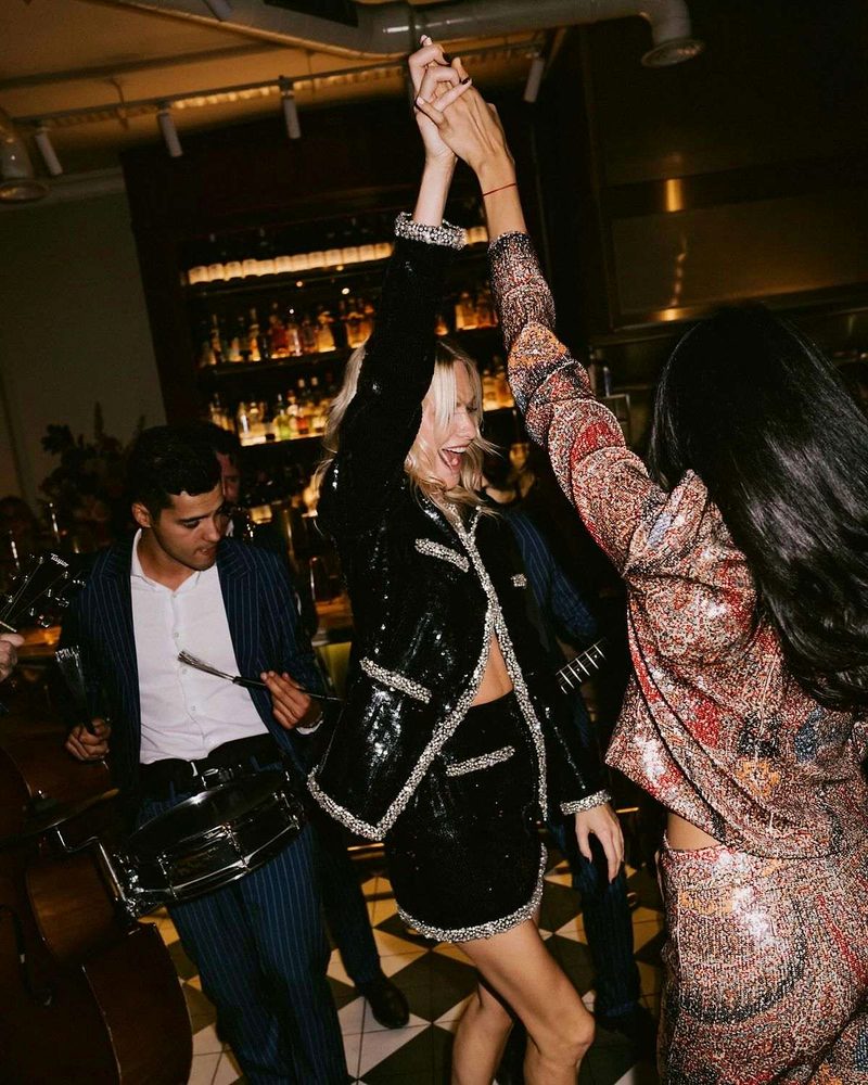 Two friends in sequins dancing with hands joined in front of a live band