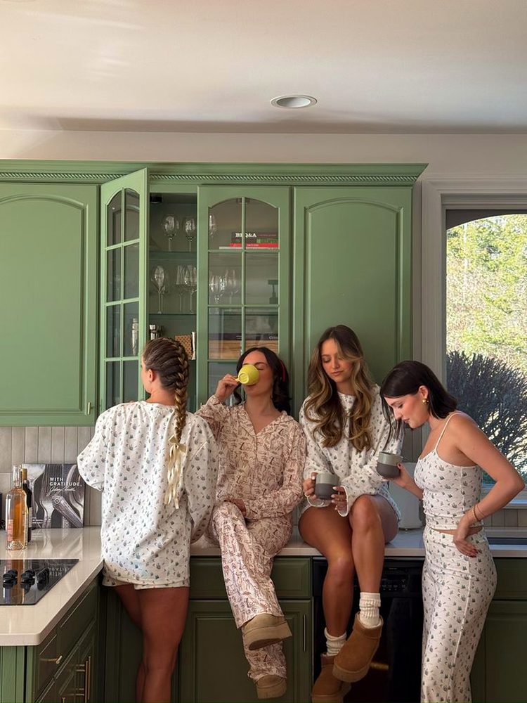 Four friends in floral pyjamas sipping coffee around a country kitchen bench
