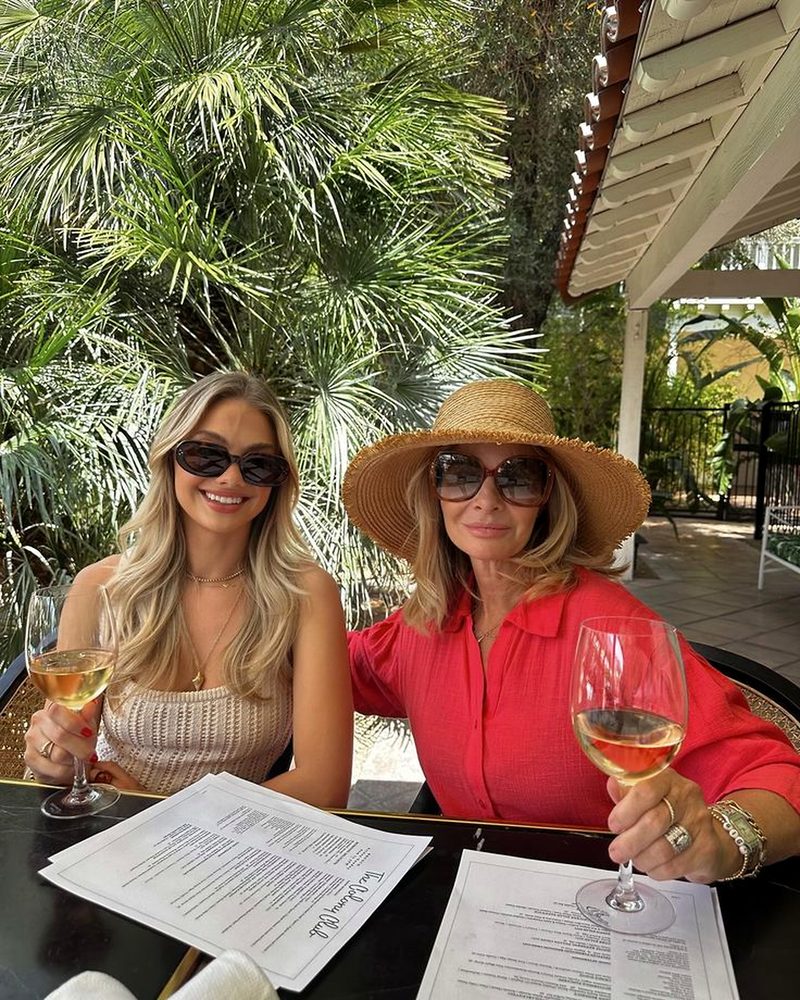 Two friends of different generations smiling over rose at a garden lunch