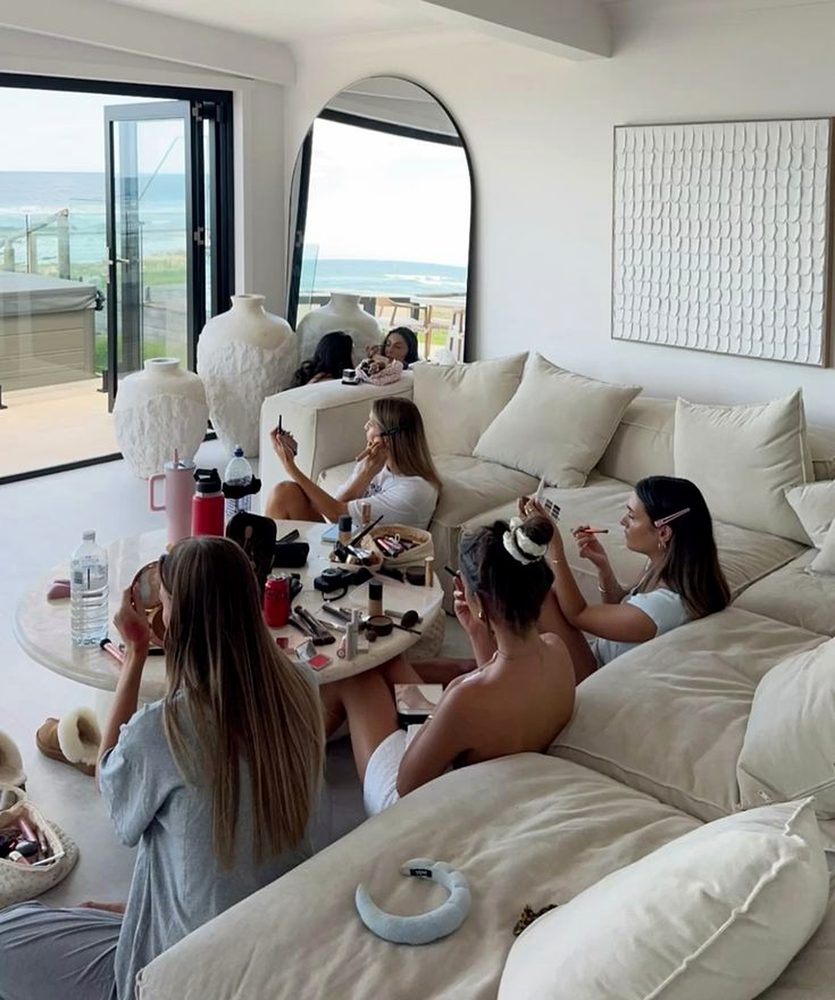 Five friends doing their makeup together on a big sofa with an ocean view