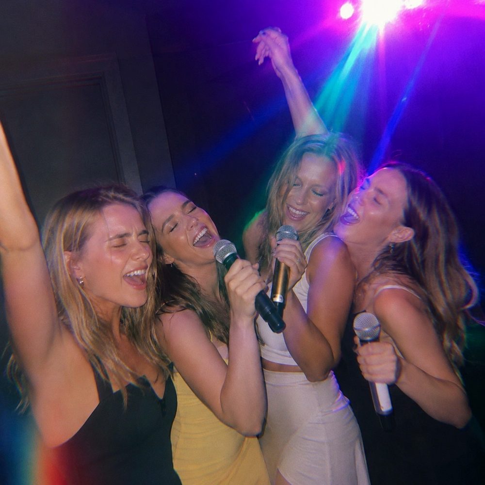 Four friends singing into microphones under disco lights