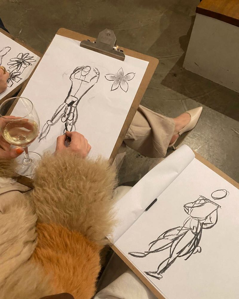 Charcoal sketches on clipboards at a life drawing class, with a glass of white wine