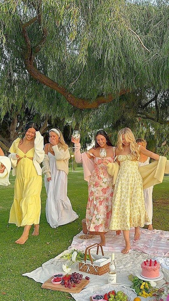 Six friends in sundresses laughing at a picnic under a willow tree