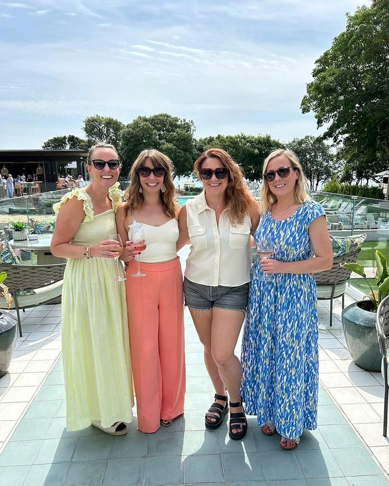 Four friends in sunglasses holding rose on a sunny resort pool terrace