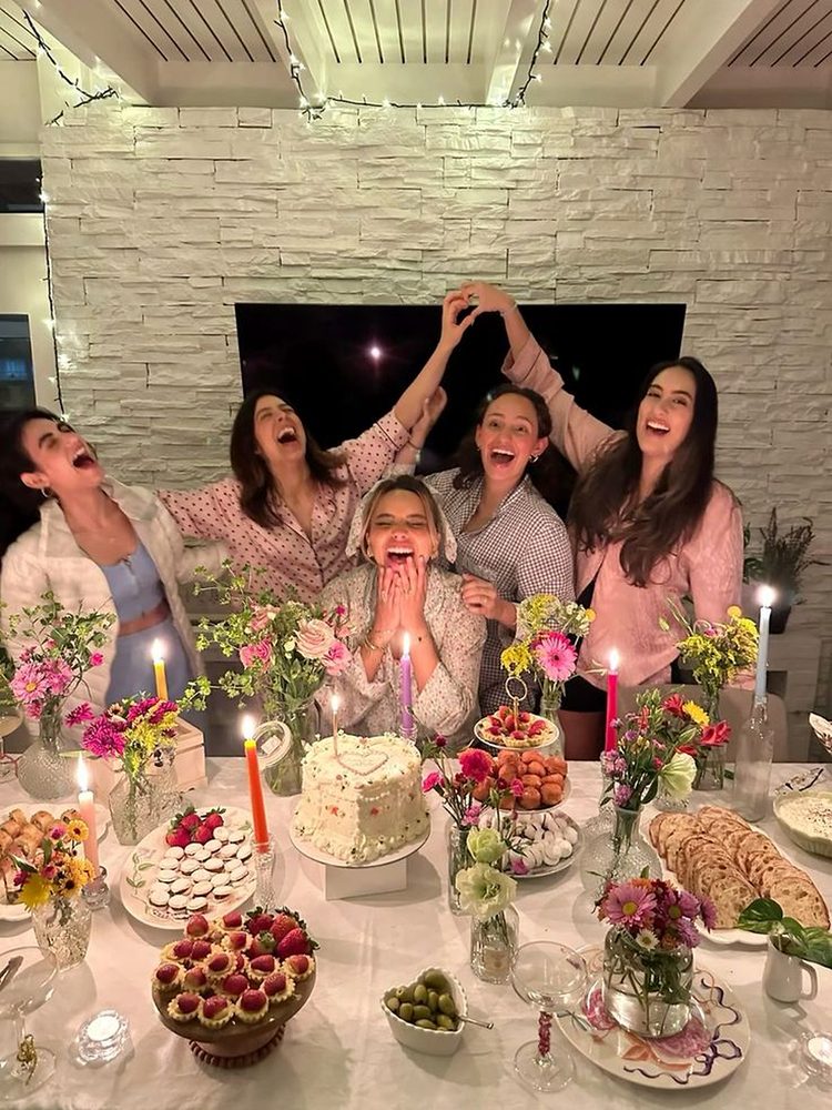 Five friends in pyjamas celebrating around a candlelit birthday table