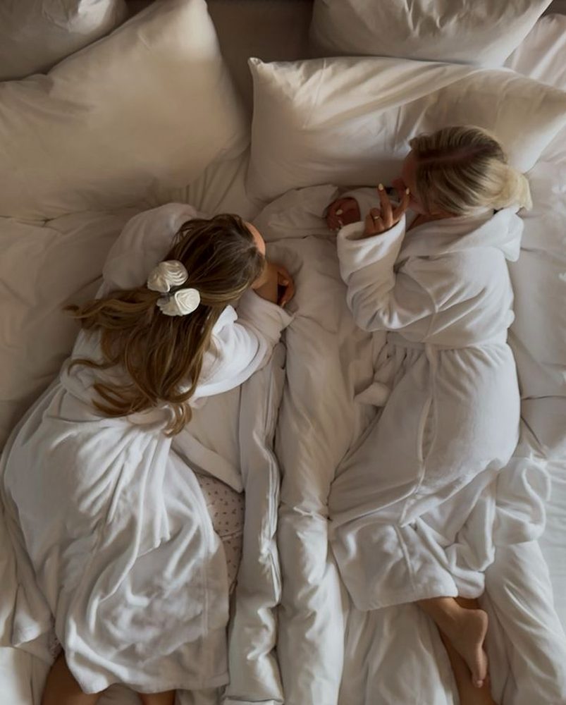 Two friends in white robes curled up on a big hotel bed
